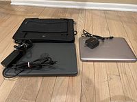 Photo of two Chromebooks closed side by side on wood floor. HP Chromebook with cover and charger on left, silver ASUS Chromebook with charger on right.