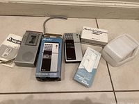 Two pocket tape recorders on floor with boxes and telephone adapter accessory, showing overall lot contents