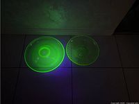 Two green uranium glass serving pieces glowing under black light, showing their distinctive bright green fluorescent appearance.