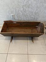 Full view of the antique wooden baby cradle showing rectangular body with two curved wooden rockers and distressed wood surface.
