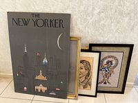 Various art pieces including The New Yorker poster on board and arranged framed prints leaning against wall.