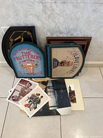 Photo showing framed wood paintings with vintage signage style artwork and a few miscellaneous prints on the floor