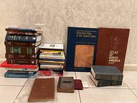 Overview photo showing two large atlases, a stack of assorted older books and business books including a leather-bound book, placed on the floor