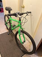 Front angled view of bike showing green frame, black handlebar grips, and front wheel knobby tire.