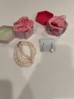 Freshwater pearl bracelet with three strands laid next to two decorative gift boxes and a pair of earrings on a card labeled 925 Sterling Silver.