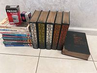 Full view of all books showing five large Chilton hardcover repair manuals with different spine colors and a thick Chilton labor guide, plus a stack of smaller Haynes manuals and two automotive parts boxes.