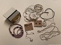 Photo showing all items in the lot including silver-tone bangles, purple stone bracelet and necklace, Monet earrings, silver-tone drop pendant and black cord necklaces, and silver-tone chain necklace.