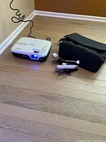 Epson projector powered on with blue light, power cord and carrying case on floor