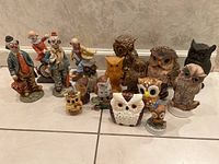 Group shot of all four clown figurines standing behind a collection of thirteen owl figurines in various sizes and materials.