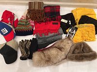 Overview showing assorted hats, scarves, gloves, baseball caps, and a faux fur stole arranged on a white surface.