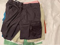 Top view showing a pile of 16 men’s shorts in various colors and styles including brown cargo and light pinstriped.