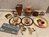 Photo showing metal serving and decorative items including trays, vase, server, and brass items aligned on floor.