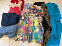 Collection of various vintage women's clothing including jeans, tops, and a dress laid out flat.