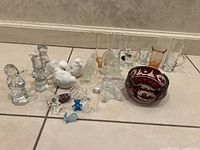 Overview of all items in the lot showing ashtray, shot glasses, glass figurines, and porcelain pigeons on a tiled floor
