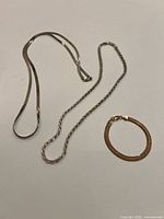 Photo showing two silver necklaces and one gold plated bracelet on a light background.