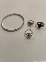 Three silver rings and one silver bracelet on a white background, showing overall lot contents.