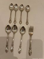 Overhead view of seven teaspoons and one salad fork arranged on white background