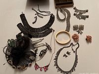 Overview of various jewelry including rhinestone necklaces, bracelets, earrings, black mesh earring hat holder with earrings attached, gold-tone bangle, and pink resin flower earrings.