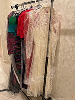 Photo showing a rack of vintage dresses covered in protective plastic including a prominent white lace wedding dress with veil, and other colorful dresses behind it.
