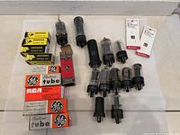 Lot showing various vintage electronic vacuum tubes with a mix of boxed and loose tubes on a white surface.