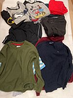 Overall view of womens clothing laid out, includes sweaters, shirts, T-shirts, black jeans. Various colors and styles shown.