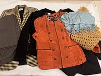 Several women's jackets and suits laid out, one orange leather jacket, black velvet jacket, suit jacket, and scarf visible.
