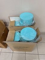 Open cardboard boxes filled with multiple aqua blue round gift boxes, each wrapped in plastic.