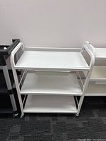 Front view of white 3-tier trolley with small plastic drawer under top shelf and caster wheels.