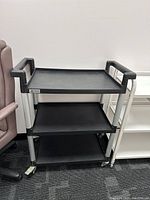 Front and side view of the black and grey three-tier trolley showing the overall structure and wheels.