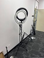 Two mounted ring lights on fully extended tripod stands, black and white colored, with cords visible, plus additional stands on floor nearby