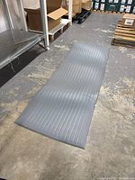 Grey ribbed anti-fatigue mat laid out on concrete floor in warehouse setting.