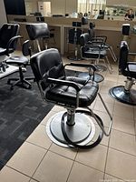 Front angle view of the single used black leather barber chair showing padded seating, armrests, and chrome base with footrest.