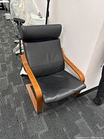 Front view of black leather chair with wooden body, fabric support visible underneath.