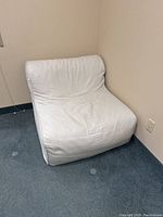 Side-angle view of the light beige lounge chair showing its curved cushion and fabric upholstery in a corner room.