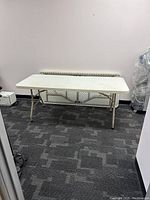 White folding table set up with beige metal folding legs, rectangular top.