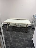 Front view of the white folding table set up in room on gray patterned carpet.