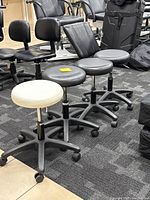 Four rolling task stools arranged in a row on carpeted floor showing one white stool and three black stools from front angle.