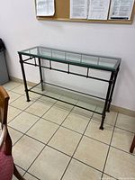 Glass console table full view against wall showing clear glass top, metal frame, and lower glass shelf.