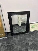 Front view of the large decorative mirror leaning against a wall, showing the textured black frame.