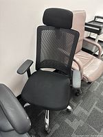 Front view of black mesh office chair with adjustable headrest and armrests, showing padded seat and chrome wheeled base.