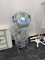 Full view of the gray Soliftron photo facial machine covered in clear plastic standing on a carpeted floor beside other medical equipment.