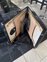 Open massage table showing wooden legs and frame with adjustment wires and mechanisms inside, carrying case partially visible.