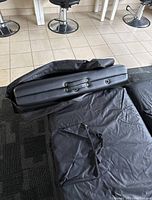 Folded black portable massage table with visible handle and leg attachment hardware, partially inside carrying case on carpet.