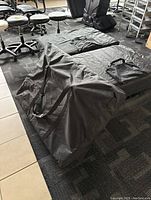 Portable black massage table in black fabric carrying case on office carpet floor
