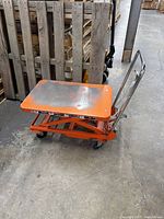 Side view of orange hydraulic scissor lift table cart showing scissor mechanism and caster wheels