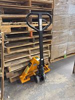 Front-side view of yellow pallet jack with black handle in warehouse environment