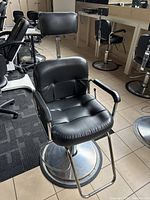 Front view of black barber chair showing cushioned seat, backrest, headrest, armrests, footrest, and metal base.