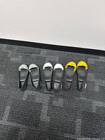 Five slip-on steel toe shoe covers lined up on carpeted floor, showing various sizes and toe cap colors (silver and yellow).