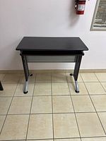 Front view of the small black office desk showing the main top surface and metal legs.