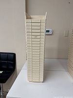Tall stack of 12 cream plastic storage bins showing front access lip and uniform stackability.